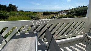 Uma varanda com vista para o mar, um corrimão branco e uma mesa com cadeira.