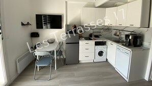 Uma cozinha compacta com armários brancos, forno embutido, micro-ondas, máquina de café e máquina de lavar.