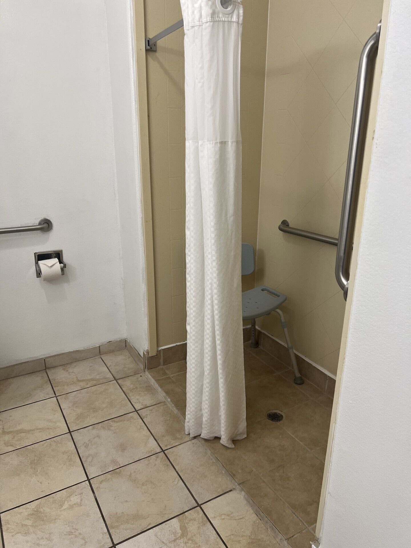 Een kleine betegelde badkamer met douchegordijn, toilet en een handgreep.