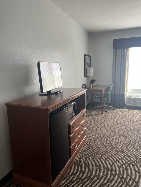 Habitación de hotel con cómoda de madera, televisor encima, escritorio con silla y alfombra estampada.