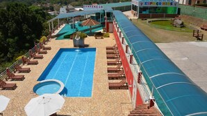 A swimming pool with lounge chairs and umbrellas, a covered area, and a building labeled "CONVENÇÃO ESPAÇO KIDS". - Hotel do Papai Noel  (Itatiaia)