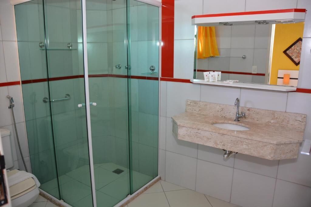 A bathroom with a glass-enclosed shower, a sink with a marble countertop, and a mirror with a red frame.