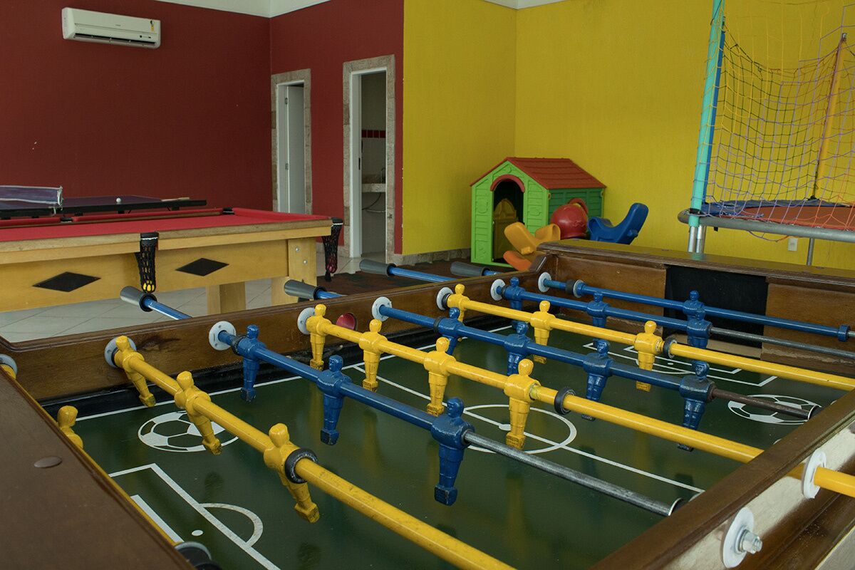 Uma mesa de futebol de mesa em um quarto com paredes vermelhas e amarelas, uma casinha de brincar e uma mesa de pingue-pongue.