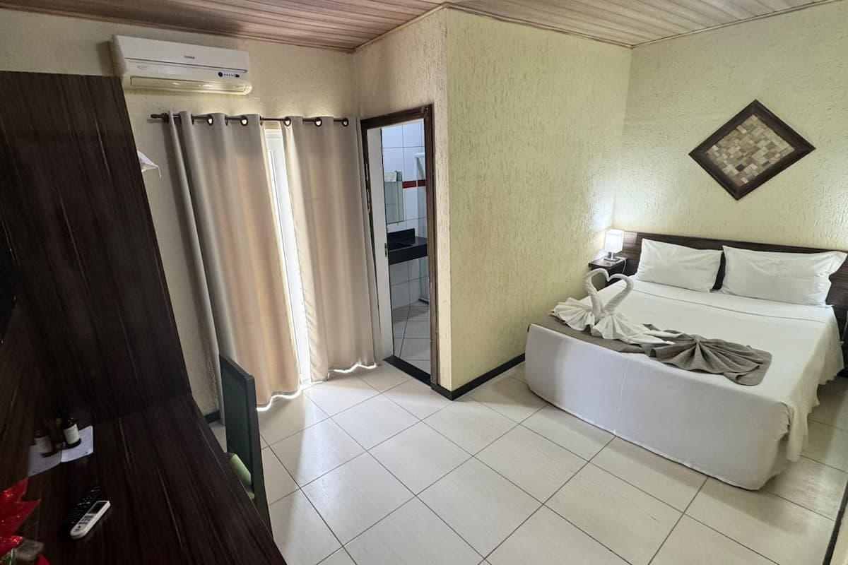 Ein Hotelzimmer mit Bett, kleinem Tisch, Nachttisch, Spiegel und Fenster mit Vorhängen.