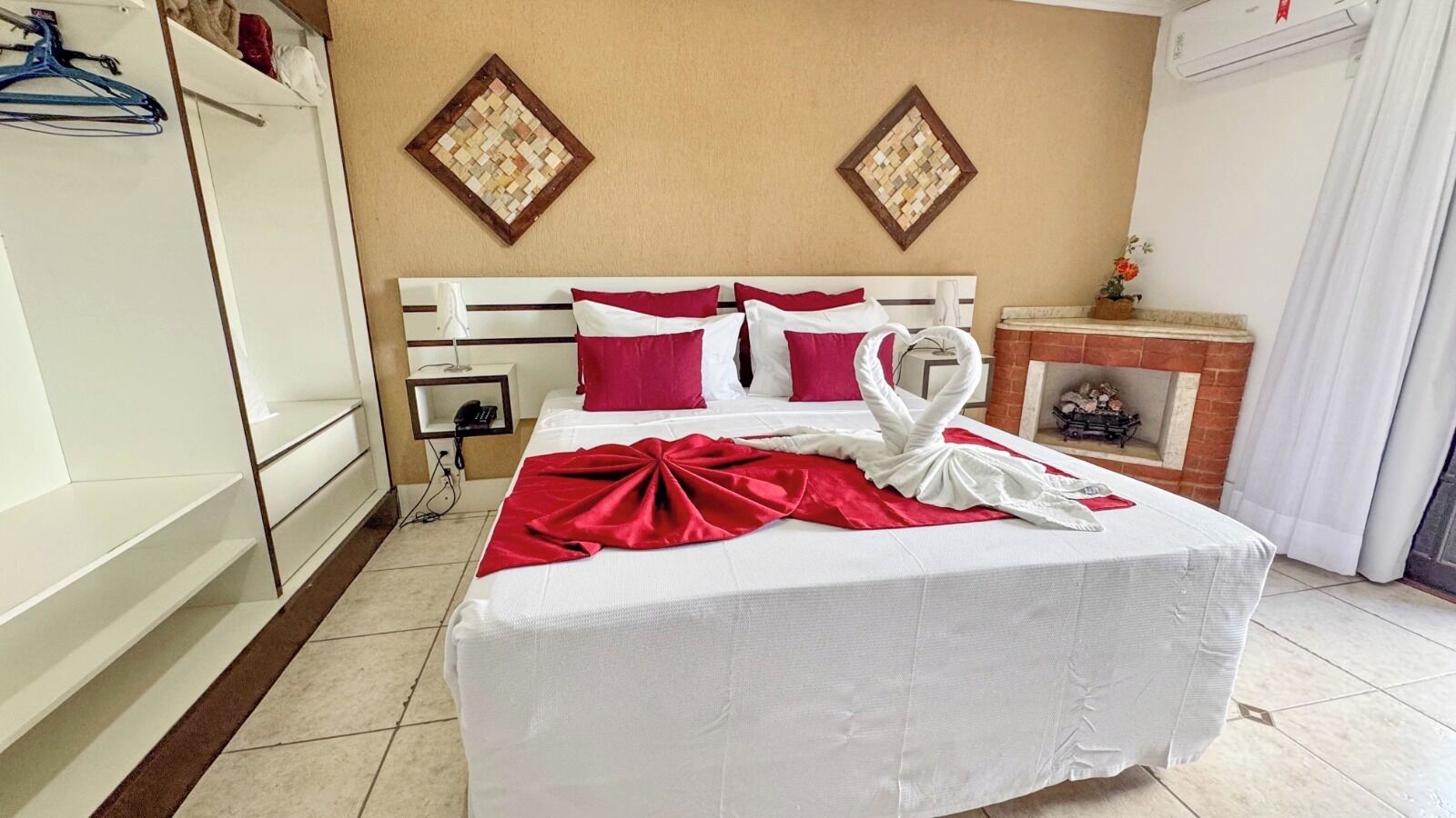 A hotel room with a bed, a wardrobe, a small table with a vase, and a fireplace.