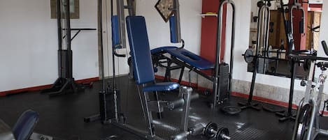 Un gimnasio con diverso equipo de ejercicio, incluyendo una prensa de banca, una estructura para sentadillas y pesas sueltas.