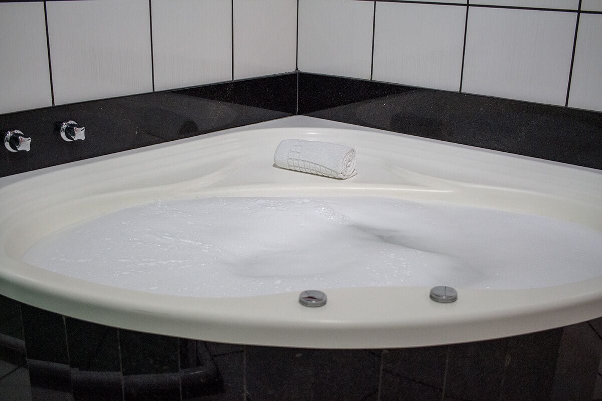 Una bañera con toalla blanca, grifería cromada y paredes de azulejos negros.