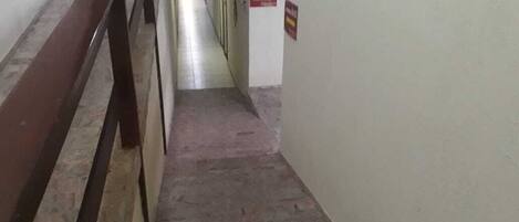 Un pasillo estrecho con una barandilla metálica a la izquierda y un cartel en la pared derecha.