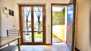 A room with a wooden table, chairs, a sliding glass door leading to a balcony, and a door to the right. - Two-room apartment with private garden 4 km from Marmore Falls. (Terni)