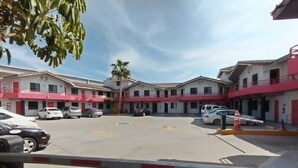 A gated parking area with multiple cars parked in front of a building with red and white exterior walls. - LIZVAN HOTEL MOTEL  (Tijuana)