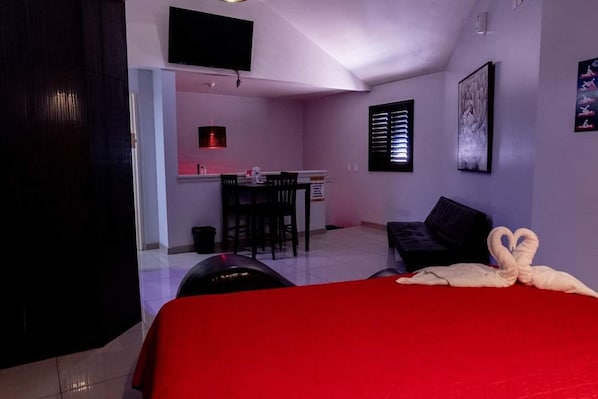A hotel room with a red bed, a desk with chairs, a TV mounted on the wall, and a painting. - LIZVAN HOTEL MOTEL (Tijuana)