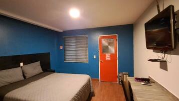 Una habitación con una cama, un escritorio, un televisor y una puerta con ventanal.