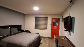 Una habitación de hotel con una cama, un escritorio, un televisor y una ventana con persianas.