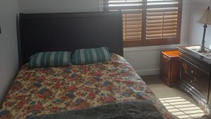 Een slaapkamer met een bed, een plafondventilator, een raam met zonwering, een nachtkastje en een kledingkast.