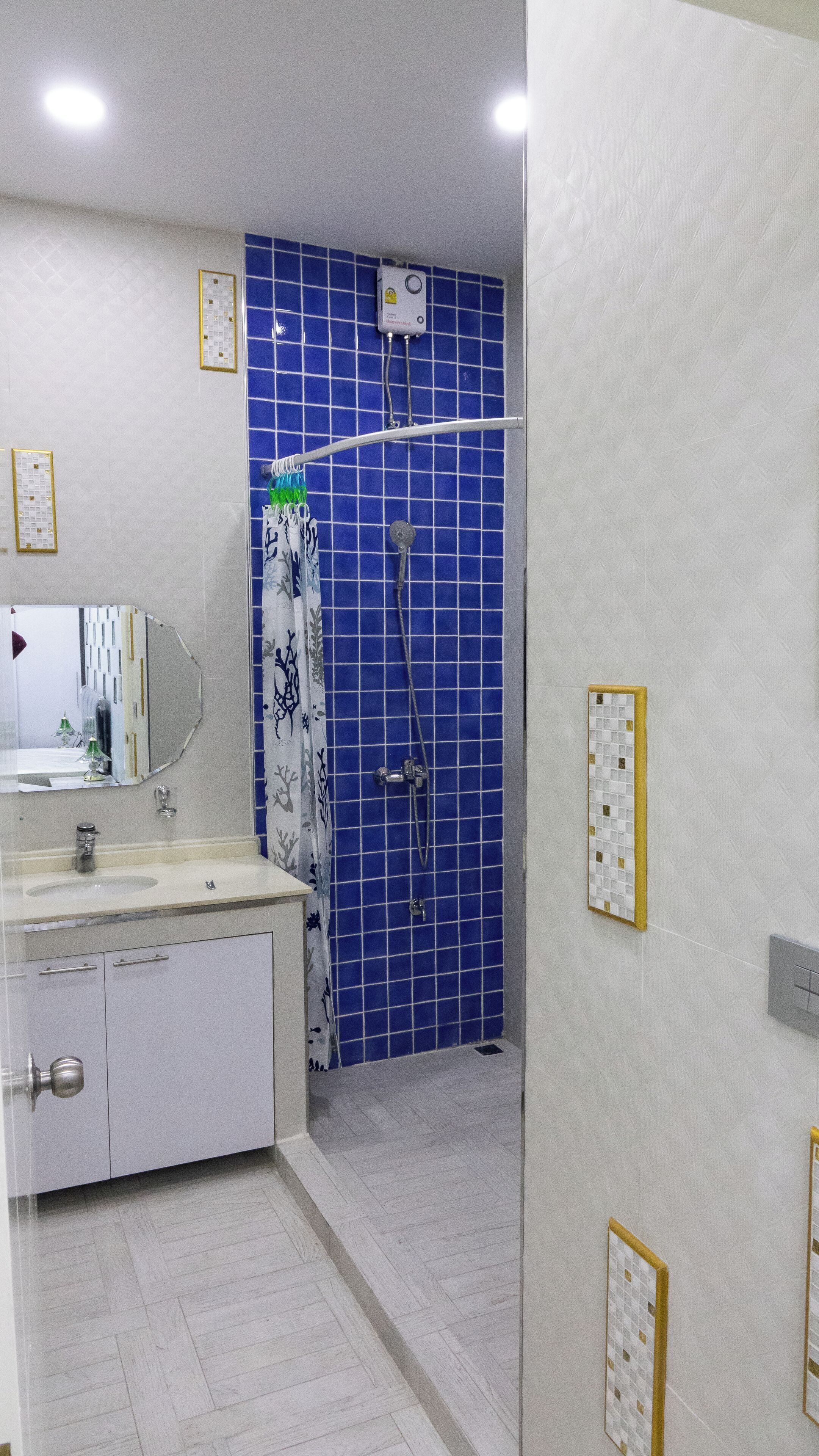 A bathroom with a white sink, mirror, and cabinets, a shower with blue tiles, and a white floor.