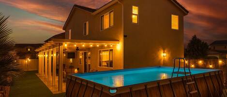 A two-story house with a swimming pool, outdoor lighting, and a covered patio area.