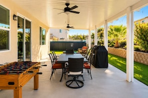 Un patio exterior con mesa de futbolín, una parrilla y una zona de comedor con sillas y una mesa.