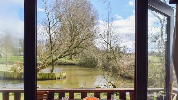 A wooden deck with a table set for two, overlooking a calm river and trees. - Woodpecker Lodge - UK49149 (Singleton, near Poulton-Le-Fylde)