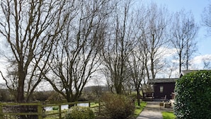 A pathway leading to a rustic building with a pond in the background. - Woodpecker Lodge - UK49149 (Singleton, near Poulton-Le-Fylde)
