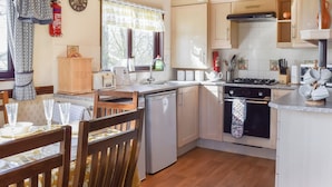 A compact kitchen with a dishwasher, stove, and a dining area with a table set for two. - Woodpecker Lodge - UK49149 (Singleton, near Poulton-Le-Fylde)