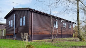 A wooden cabin with a sloped roof, a chimney, and a small porch. - Woodpecker Lodge - UK49149 (Singleton, near Poulton-Le-Fylde)