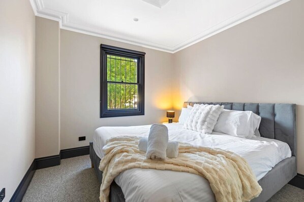 Een slaapkamer met een bed, een raam, een nachtkastje en een lamp.