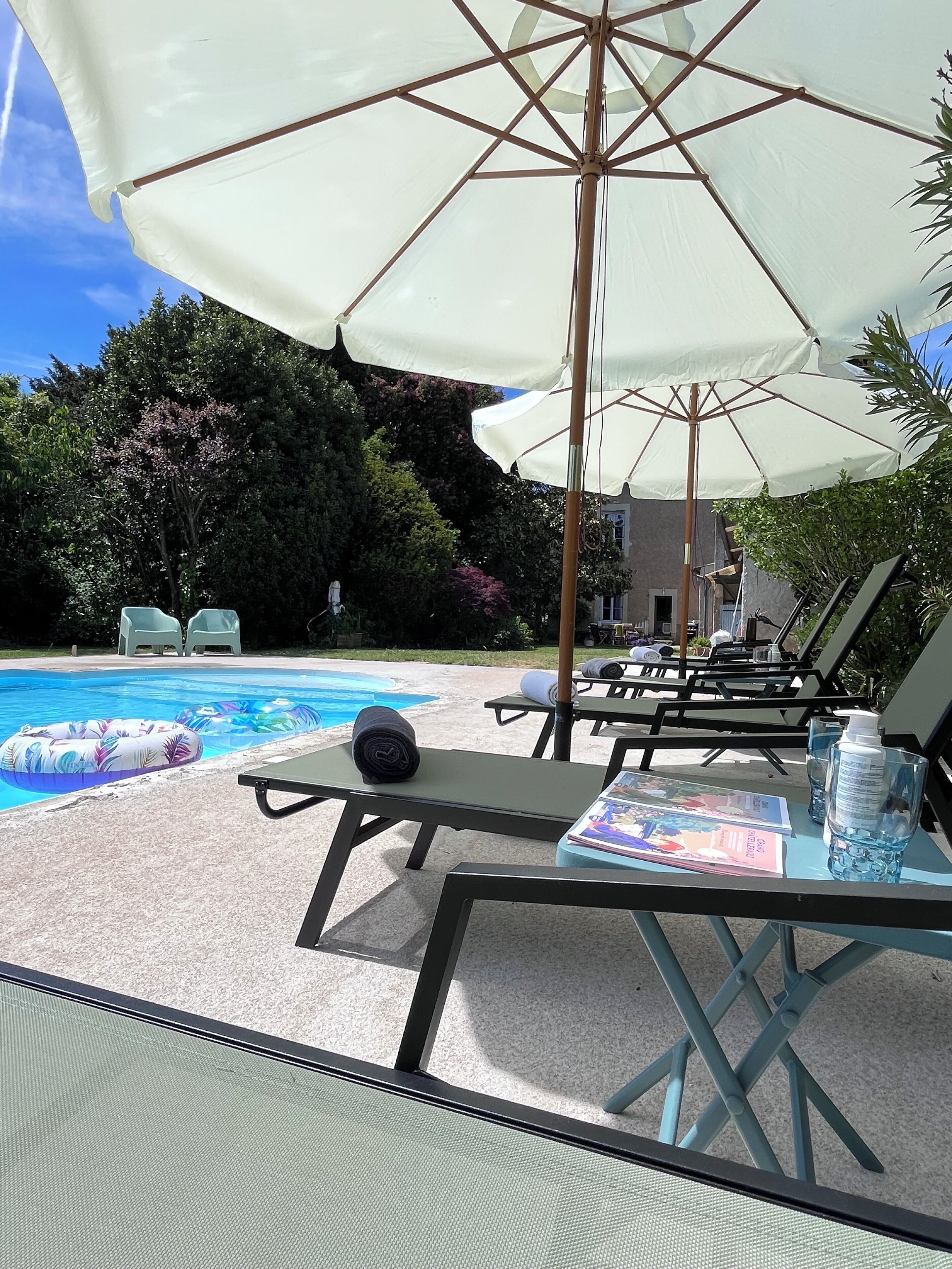 Un espace aménagé au bord de la piscine, avec des chaises longues, des parasols et une piscine.