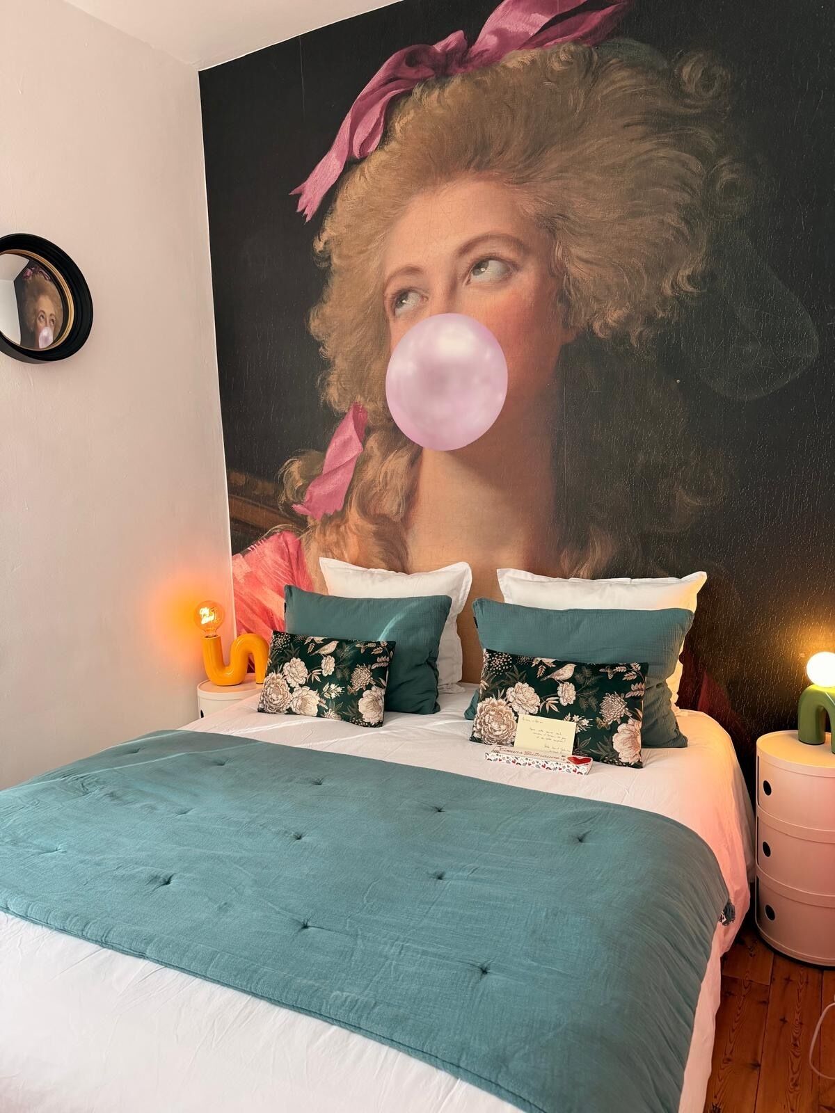 A bedroom with a large bed, two pillows, a bedside table, and a wall-mounted mirror.