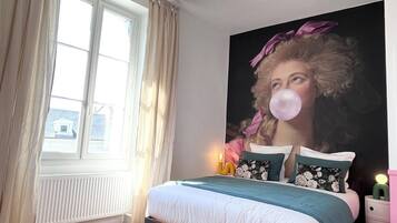 A bedroom with a large bed, a window with curtains, a wall-mounted light fixture, and a painting.