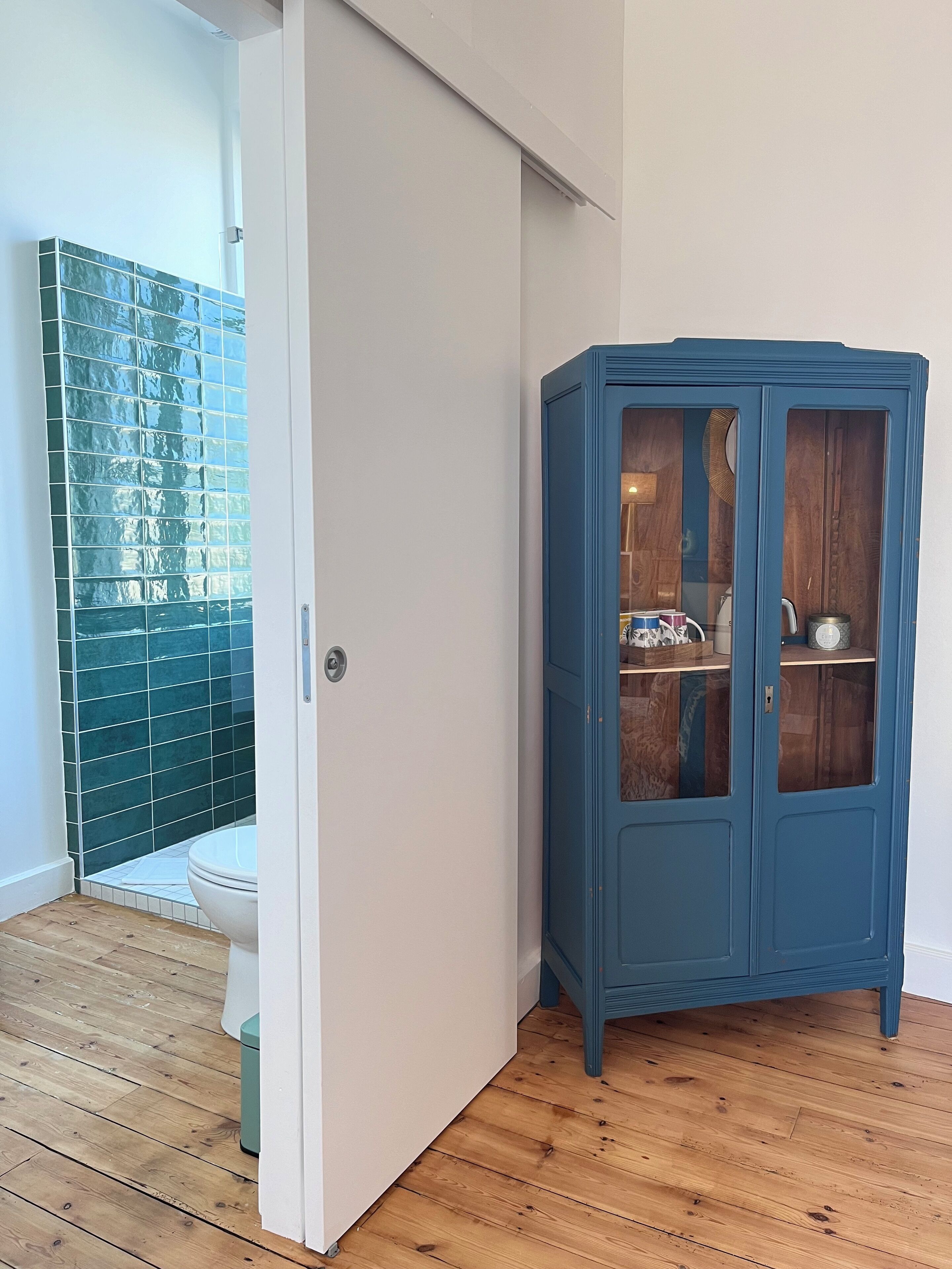 A bathroom with a wooden floor, a white toilet, and a blue cabinet with glass doors.