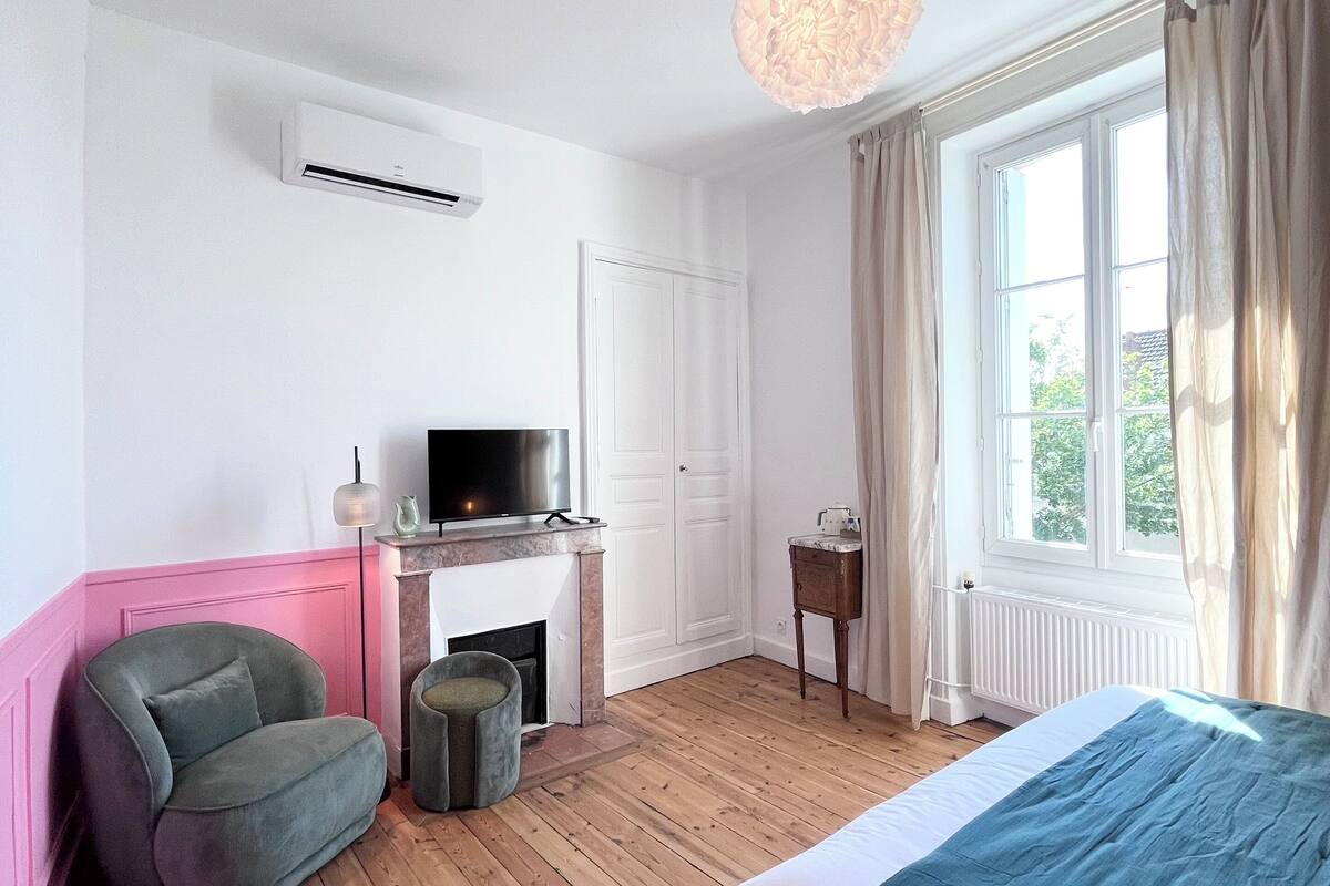 A bedroom with a bed, a television, a fireplace, a chair, and a window with curtains.