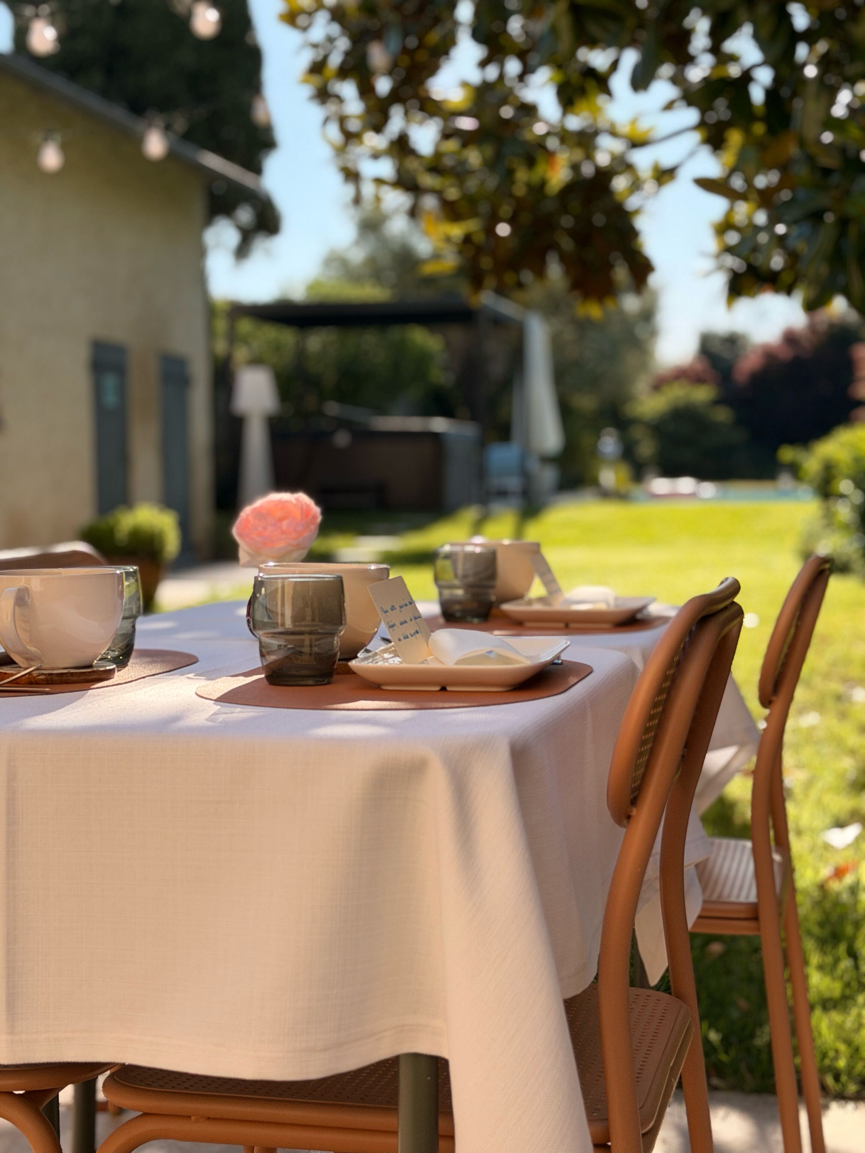 Una mesa al aire libre con mantel blanco, una copa, una taza y un libro.