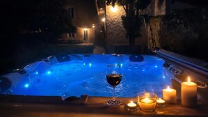 Ein Whirlpool mit einem Weinglas und Kerzen, umgeben von einer Steinmauer und Bäumen.
