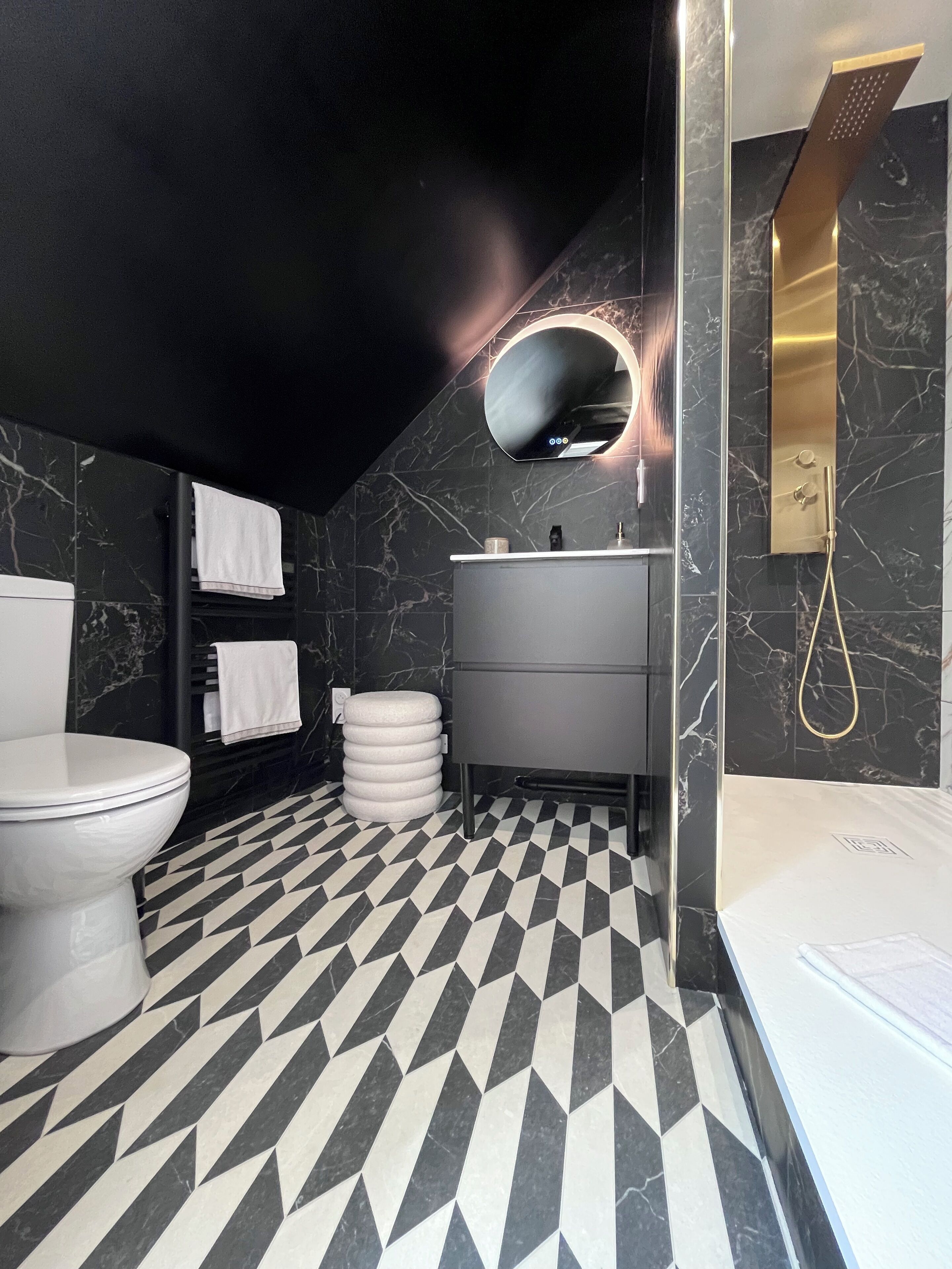 A modern bathroom with a black and white checkered floor, a white toilet, a sink with a gold showerhead, and marble walls.
