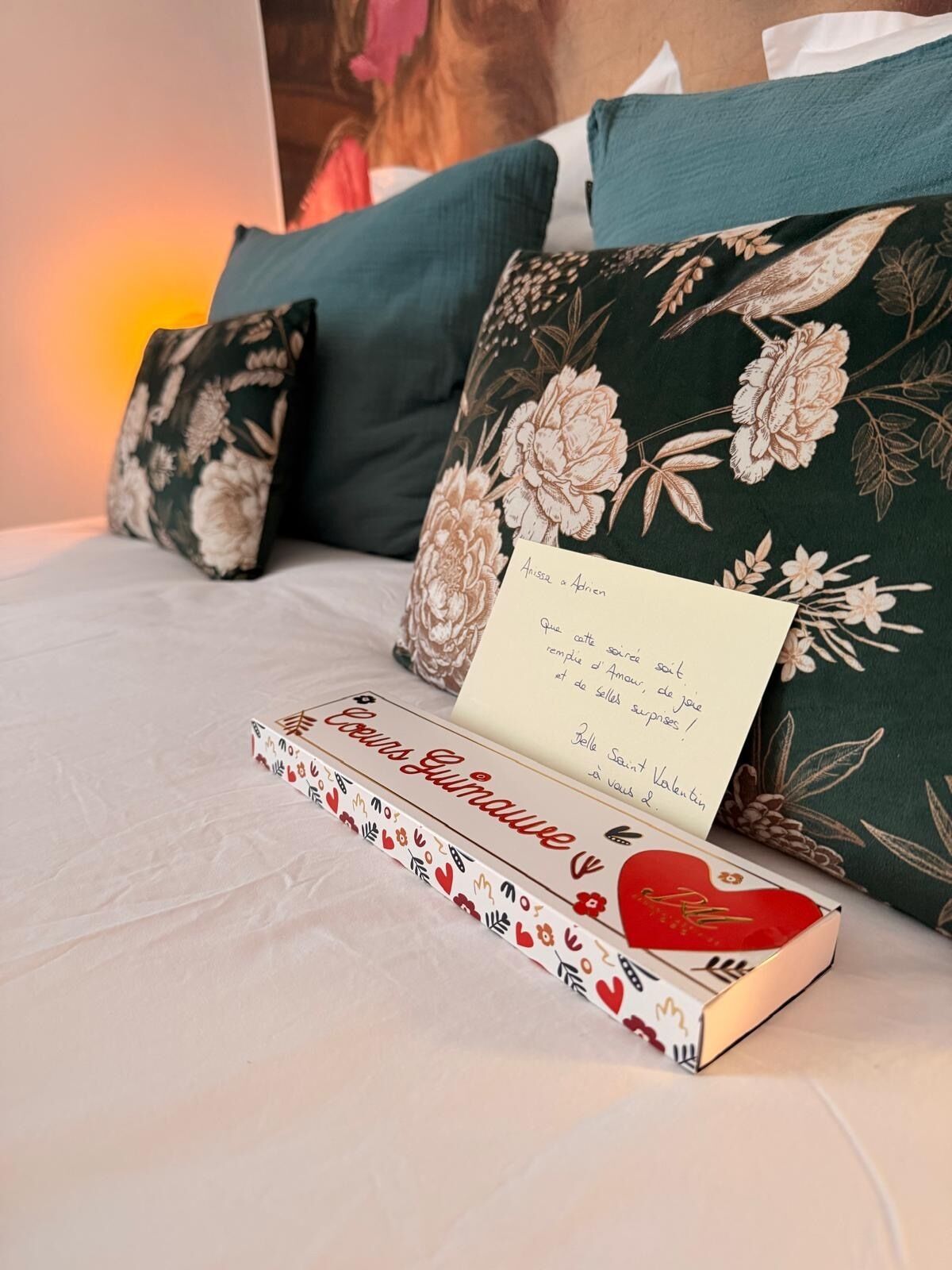 Una cama con almohadas estampadas, un libro titulado 'Cousin Gumawé' y una tarjeta con un mensaje.