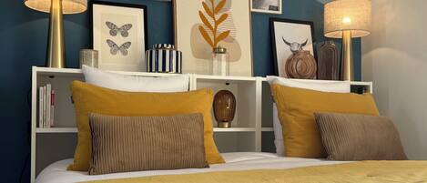 A neatly arranged bedroom with a bed, two bedside lamps, a bookshelf, and framed artwork on the wall.