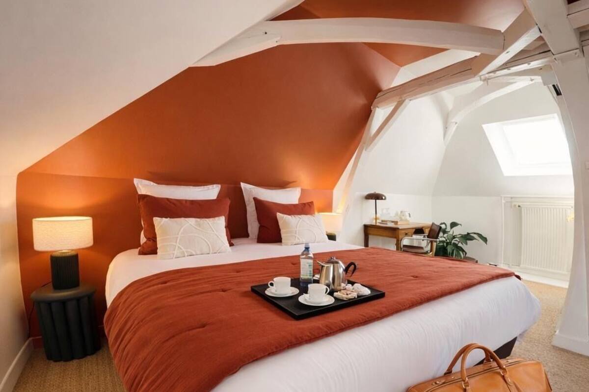 A bedroom with a large bed, a tray with tea items, a brown bag, and a desk with a lamp.