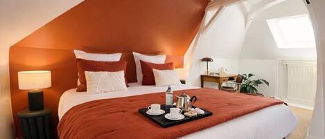 A bedroom with a large bed, a tray with tea items, a brown bag, and a desk with a lamp.