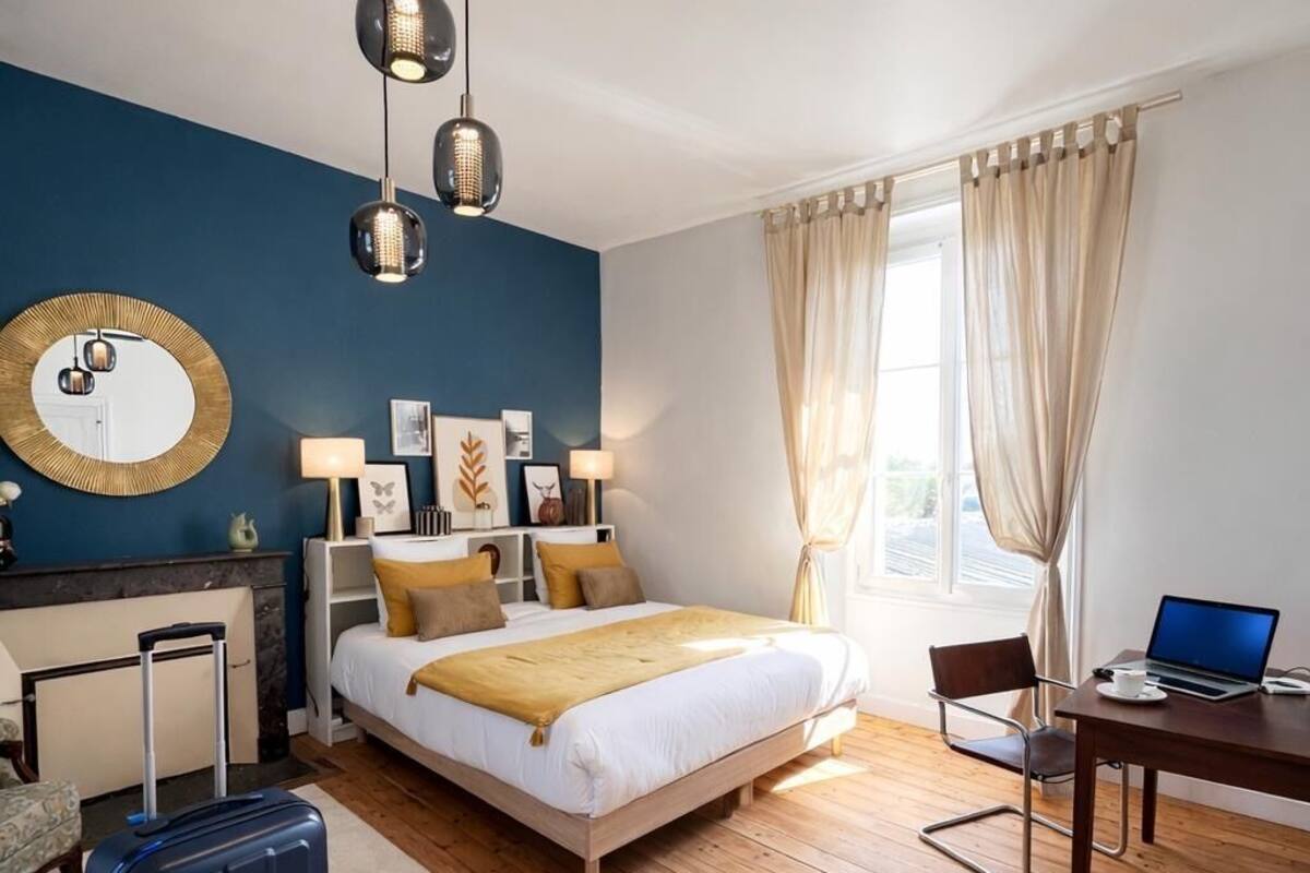 A hotel room with a bed, a desk with a laptop, a suitcase, and a handbag.