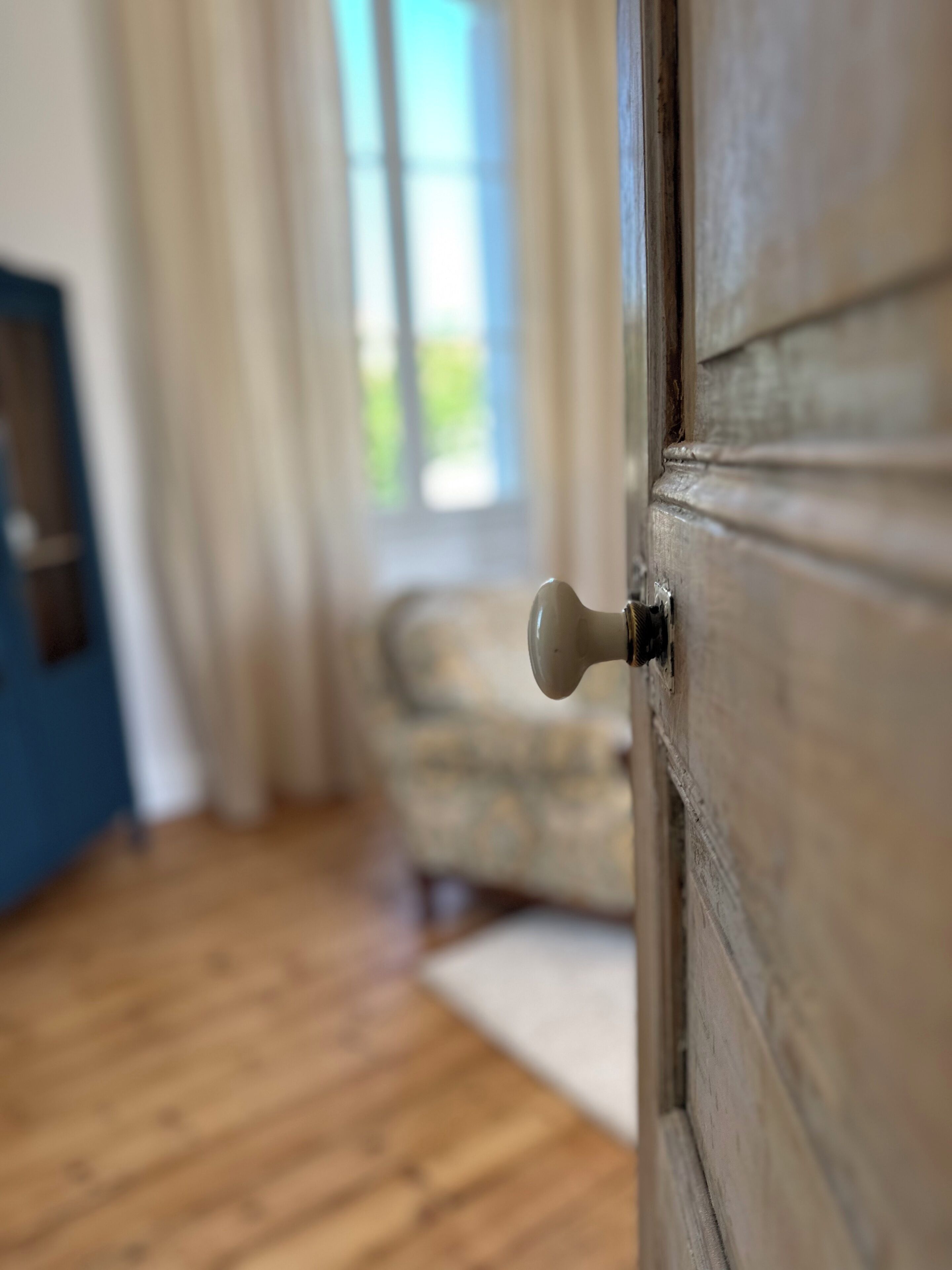 A wooden door with a round handle, a window with curtains, and a wooden floor.
