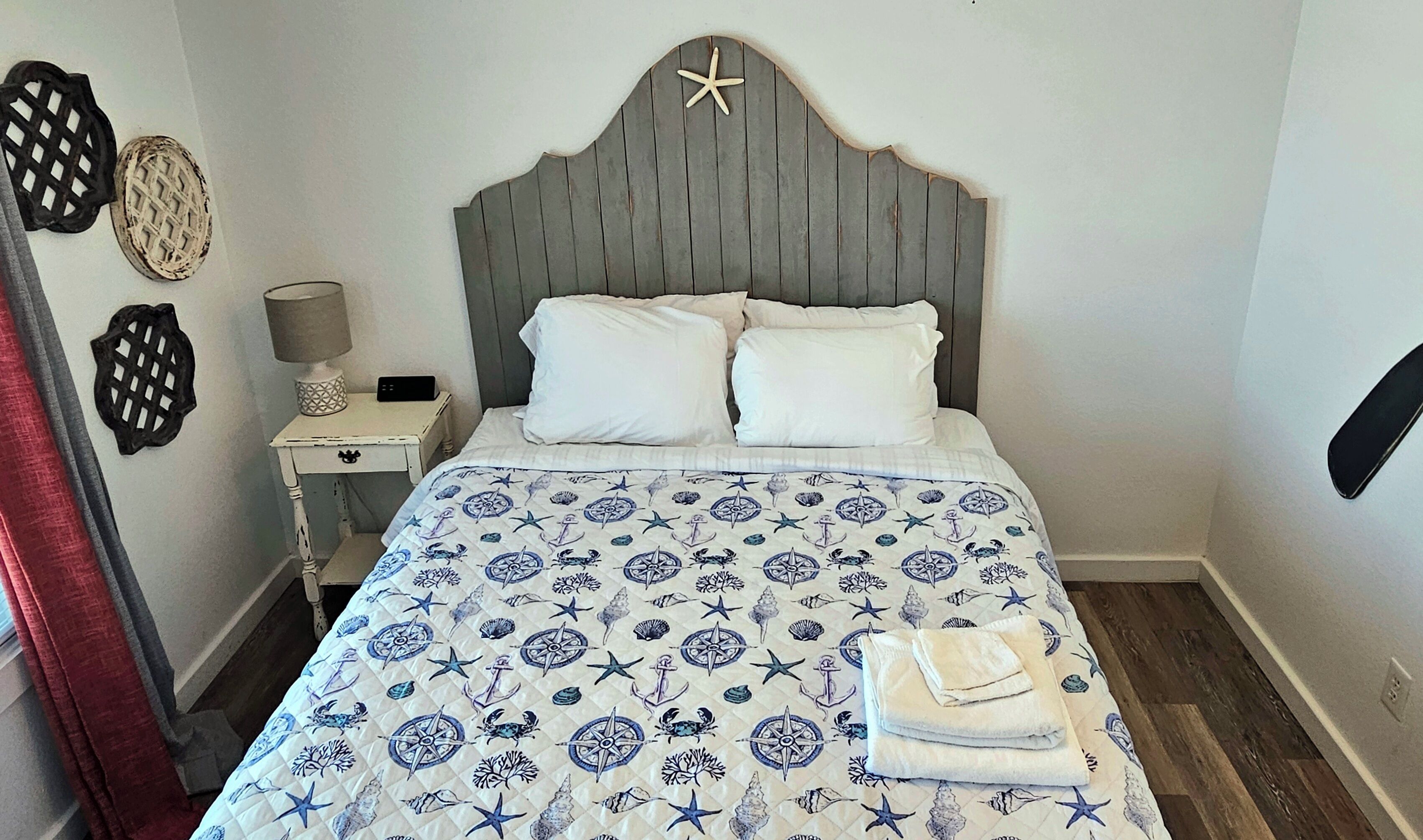 Een slaapkamer met een bed, een nachtkastje, een lamp en decoratieve muurkunst.