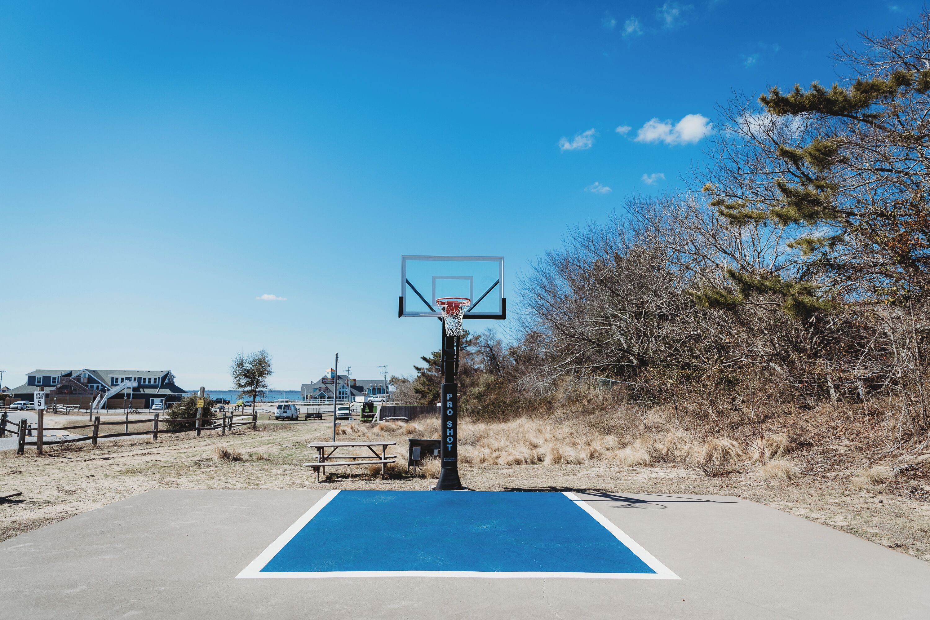 Uma quadra de basquete ao ar livre com superfície azul, uma cesta de basquete e uma mesa de piquenique.