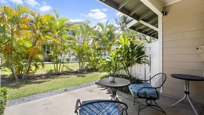 A patio with two chairs and a table, surrounded by palm trees and a view of a building.