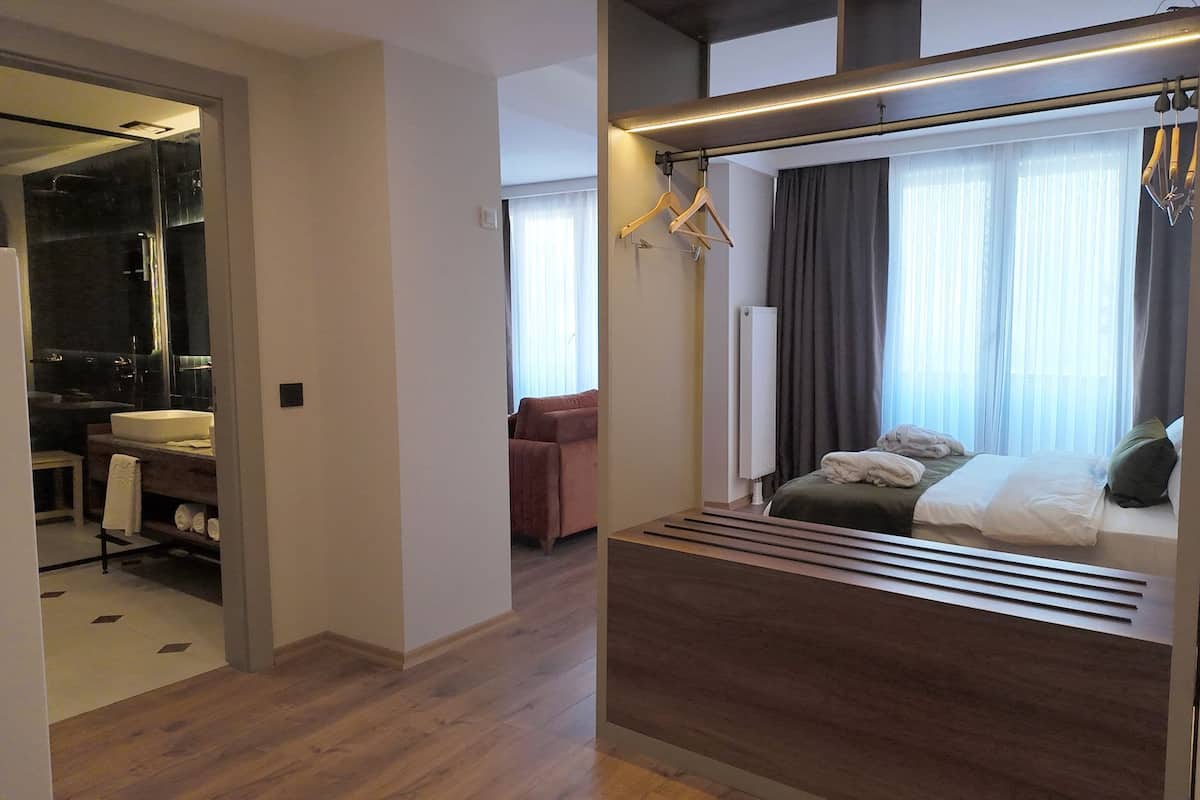 Ett modernt hotellrum med en säng, en sittgrupp, ett badrum med en stor spegel och ett trägolv.