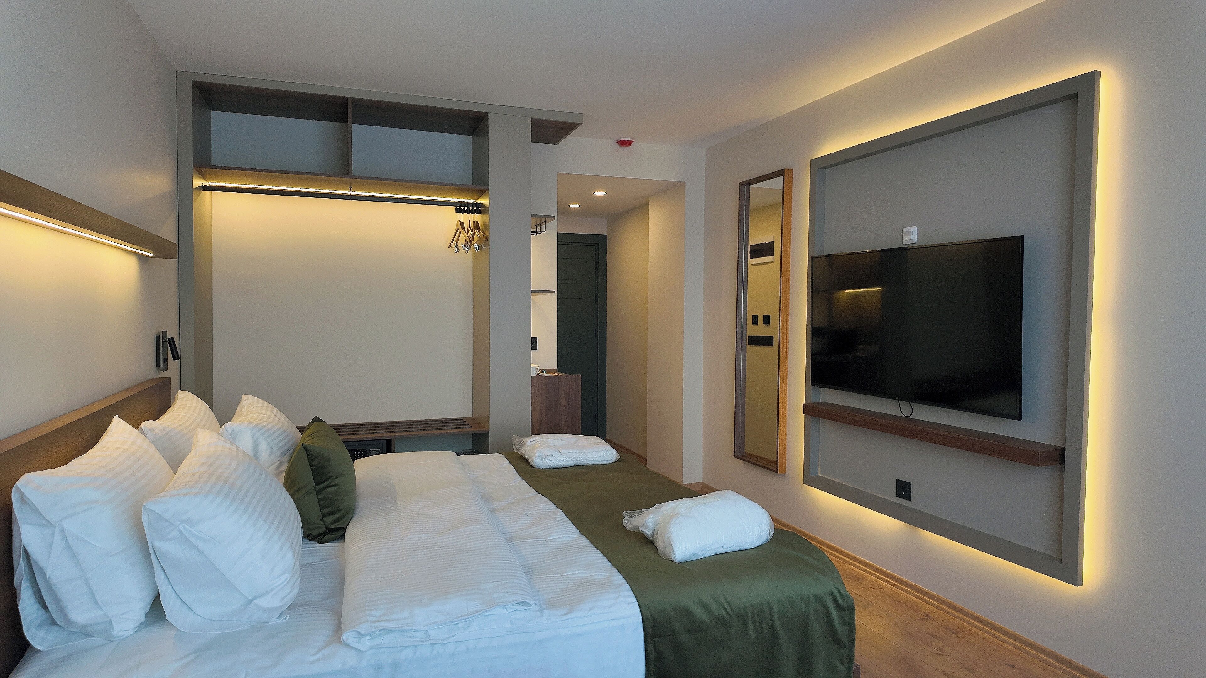 Una habitación de hotel con cama, televisión, espejo y un pequeño escritorio.