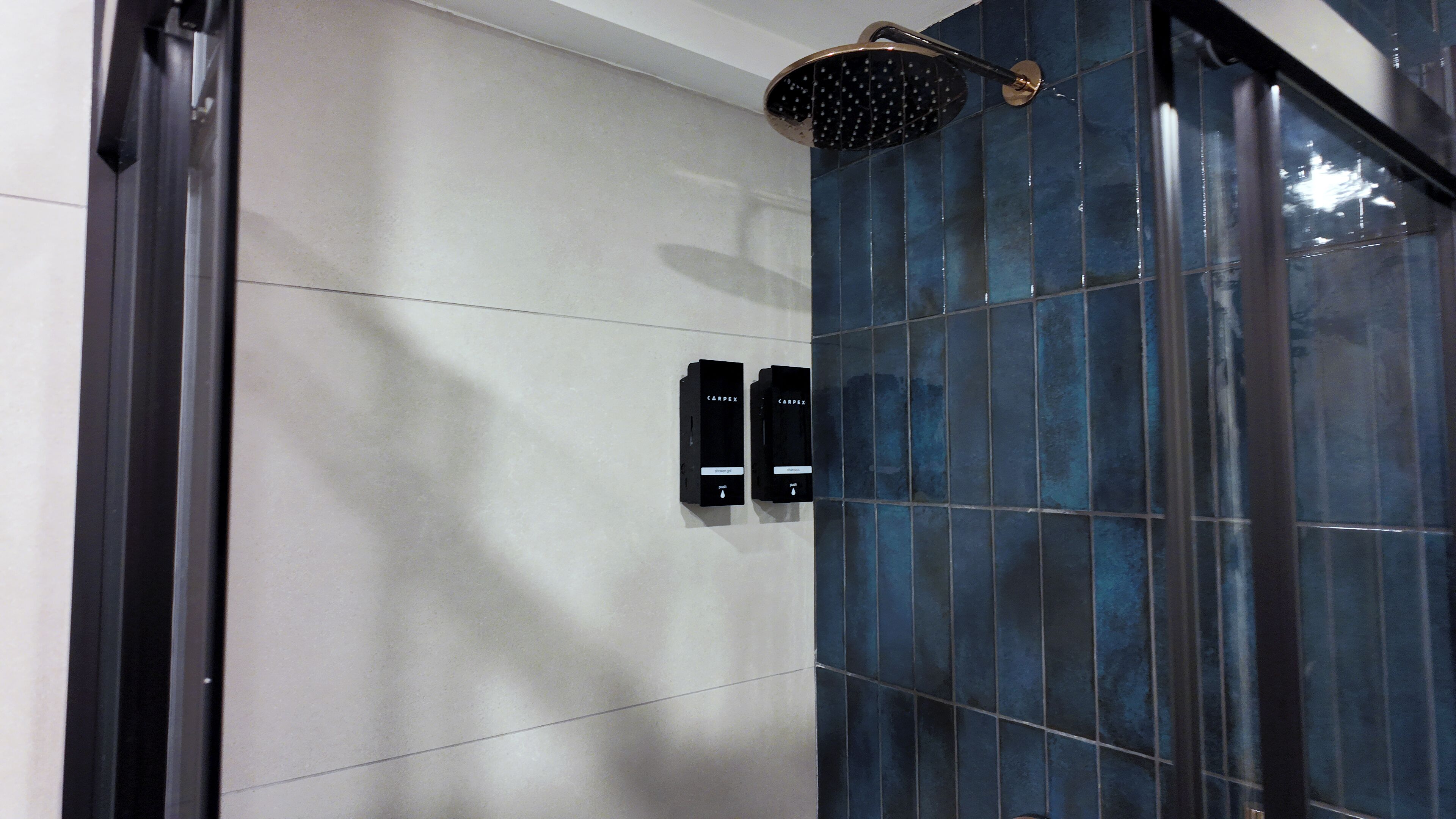 A modern bathroom with a shower, two wall-mounted hand dryers, and a glass door.