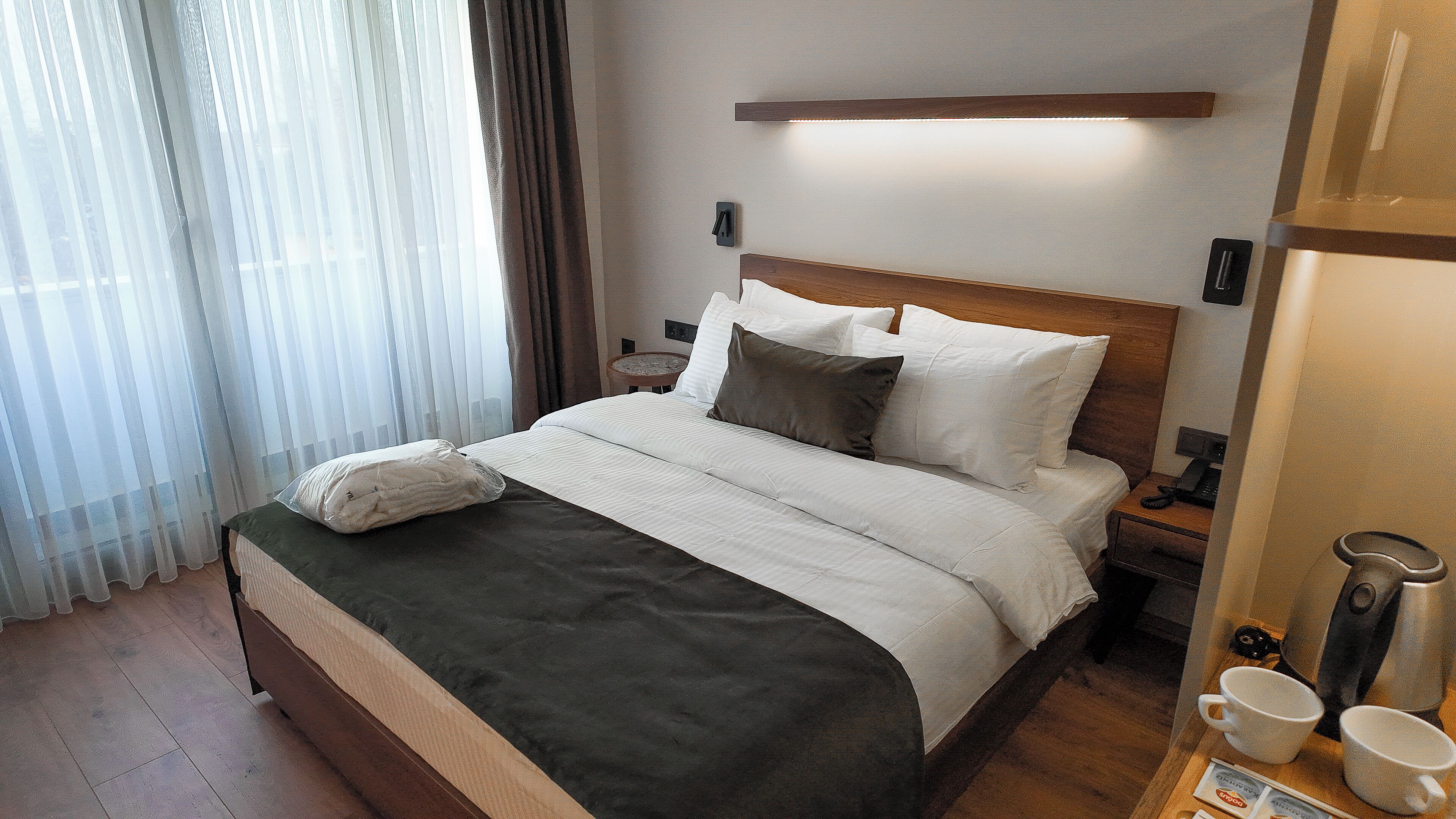 A neatly made bed with a wooden headboard, a bedside table with a lamp, and a coffee maker on the nightstand.