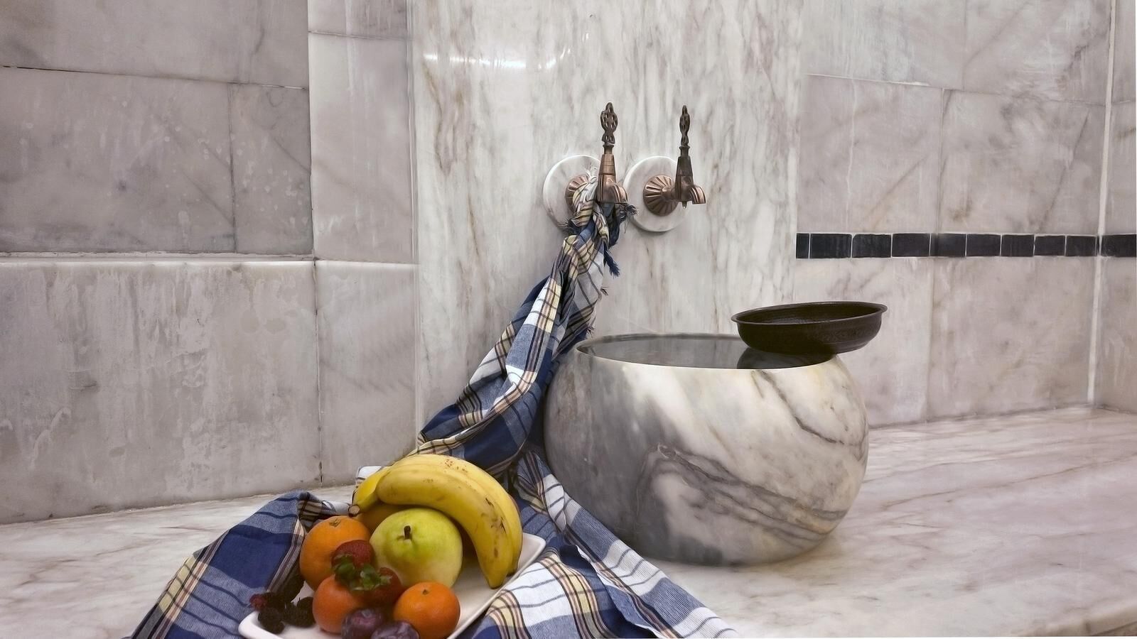Ein Badezimmer mit Marmor, ausgestattet mit einem Handtuchhalter, Handtuch, einer Schale und einer Obstschale mit Bananen, Äpfeln und Orangen.