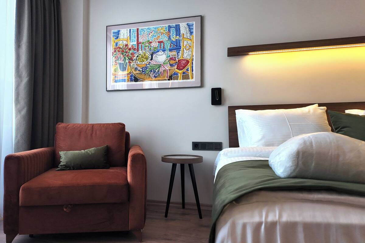 Ett hotellrum med en säng, en stol, ett litet bord och en tavla på väggen.