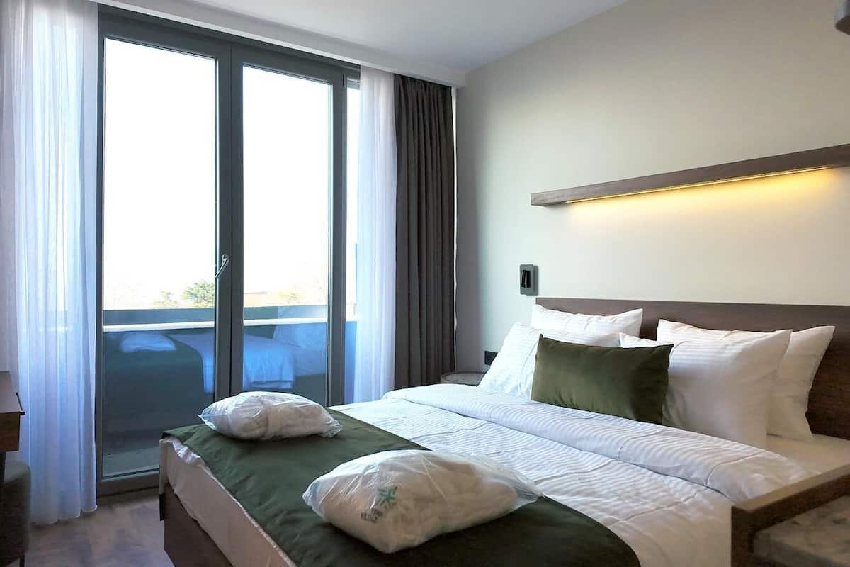 Ett hotellrum med en säng, kuddar, ett sängbord, en lampa och utsikt genom en skjutdörr i glas.